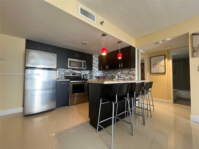 kitchen featuring backsplash, a breakfast bar, stainless steel appliances, light tile patterned floors, and hanging light fixtures