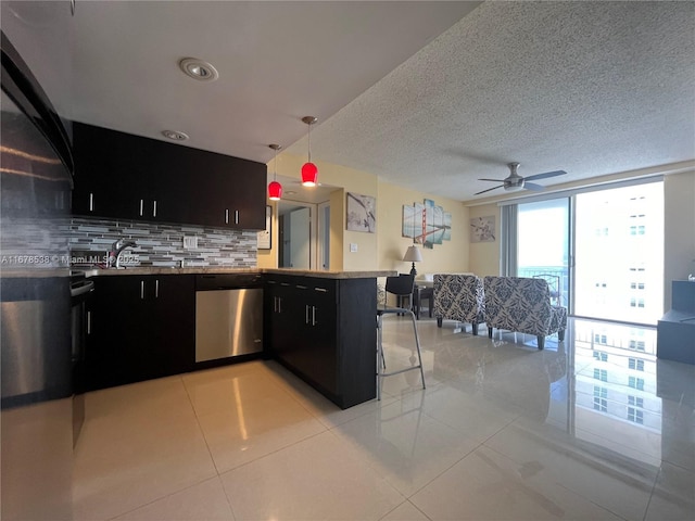 kitchen with a peninsula, stainless steel dishwasher, dark cabinetry, and decorative backsplash