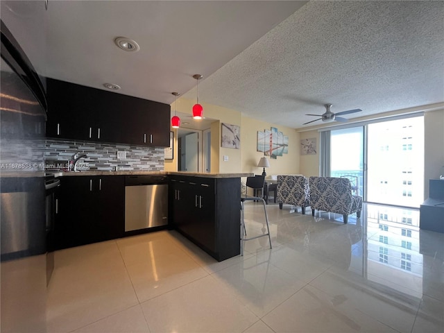 kitchen featuring dishwasher, ceiling fan, a peninsula, dark cabinets, and decorative backsplash