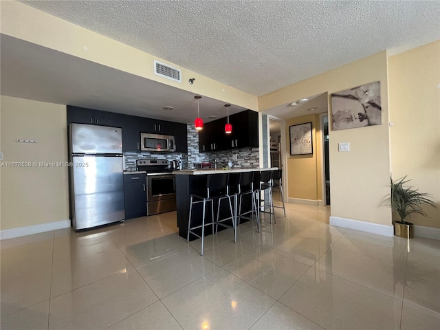 kitchen with visible vents, appliances with stainless steel finishes, a kitchen bar, dark cabinets, and decorative backsplash