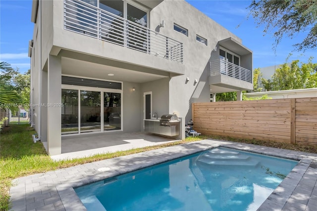 rear view of house with stucco siding, a patio area, exterior kitchen, and fence