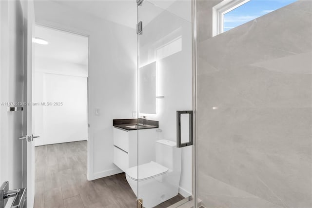 bathroom featuring toilet, wood finished floors, a shower stall, baseboards, and vanity