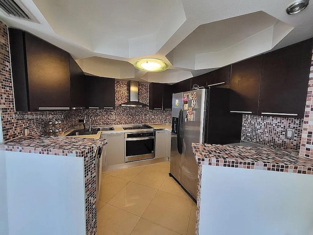 kitchen featuring decorative backsplash, wall chimney range hood, sink, light tile patterned floors, and appliances with stainless steel finishes