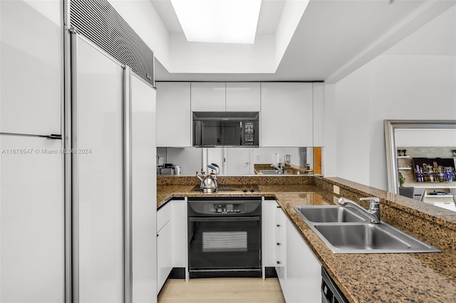 kitchen featuring white cabinets, black appliances, sink, dark stone countertops, and light wood-type flooring