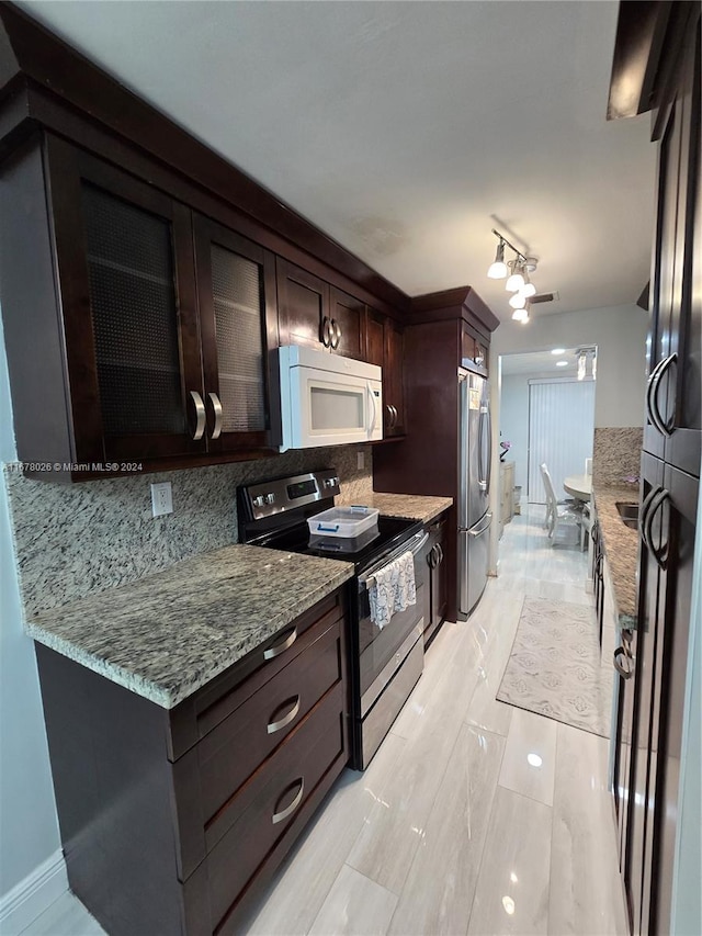 kitchen featuring dark brown cabinetry, light stone counters, stainless steel appliances, and tasteful backsplash