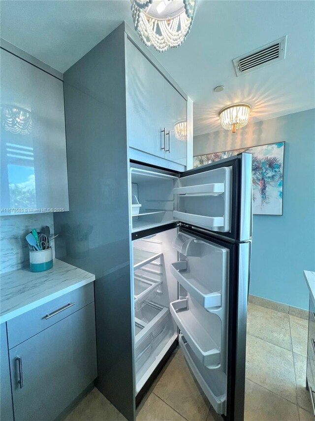 kitchen with light stone counters, light tile patterned floors, and fridge