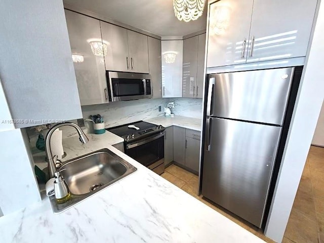 kitchen with sink, stainless steel appliances, an inviting chandelier, light stone counters, and gray cabinets