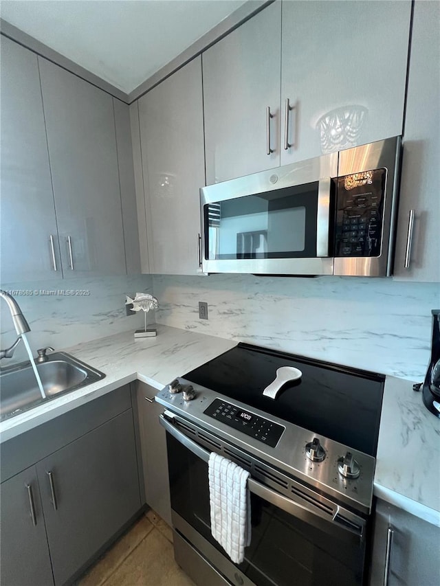 kitchen with appliances with stainless steel finishes, light stone counters, gray cabinetry, sink, and light tile patterned floors