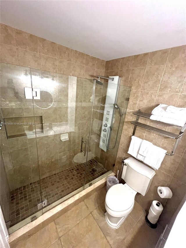 bathroom with tile patterned flooring, toilet, an enclosed shower, and tile walls