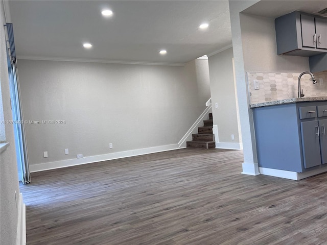 unfurnished living room with crown molding, dark wood finished floors, stairway, a sink, and baseboards