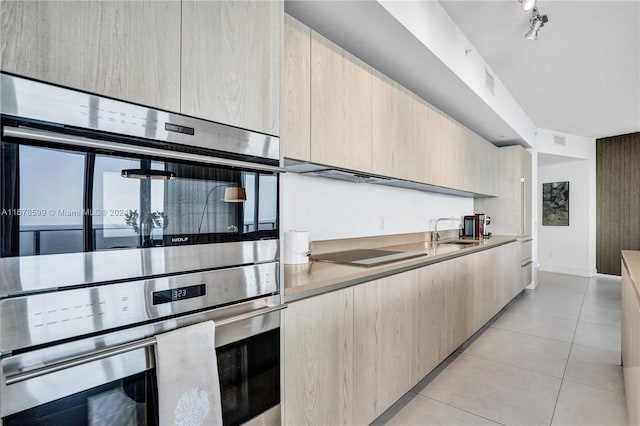 kitchen featuring sink, black electric cooktop, stainless steel double oven, light tile patterned floors, and light brown cabinets