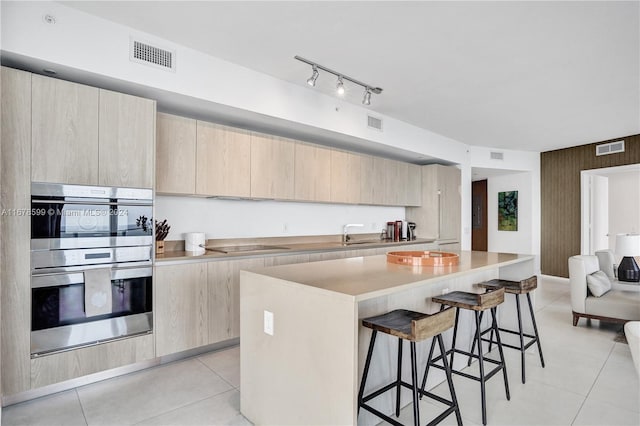 kitchen with a kitchen island, double oven, a breakfast bar, light tile patterned floors, and light brown cabinetry