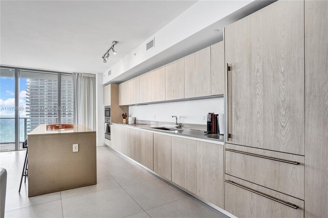 kitchen with a wall of windows, sink, light brown cabinetry, and a kitchen island