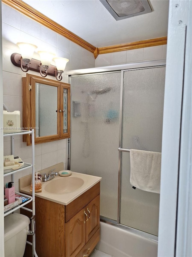 full bathroom featuring toilet, tile walls, bath / shower combo with glass door, vanity, and ornamental molding