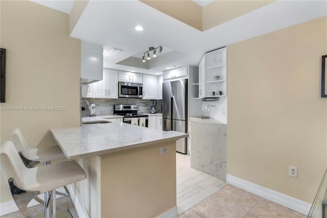 kitchen with kitchen peninsula, white cabinets, a breakfast bar area, sink, and stainless steel appliances