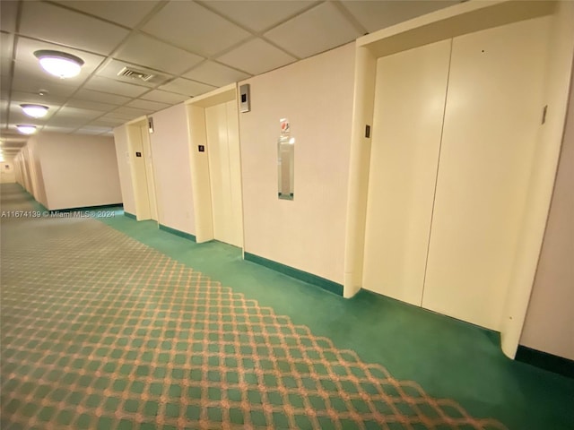 hallway featuring dark carpet and a drop ceiling