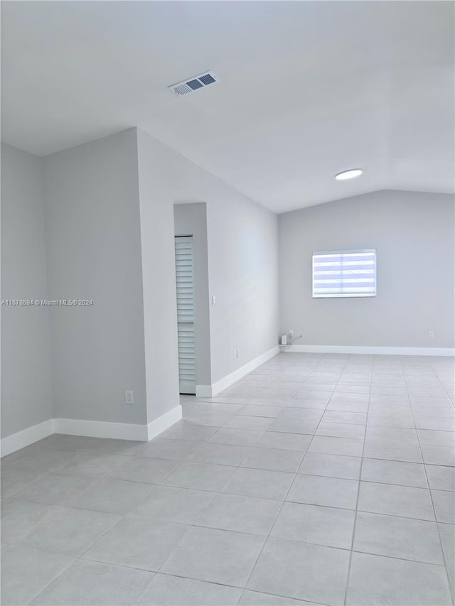 tiled spare room featuring lofted ceiling