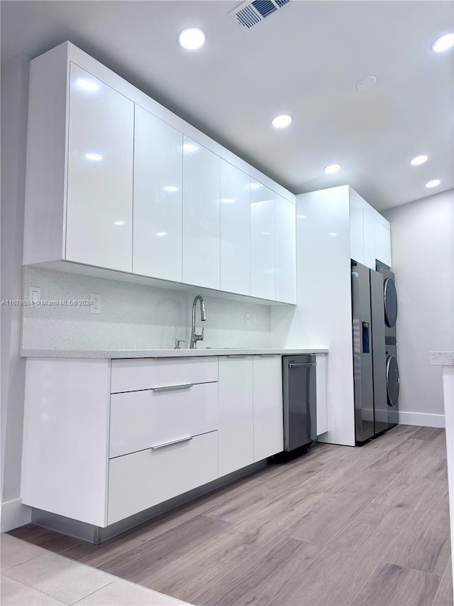 kitchen featuring sink, light wood-type flooring, stacked washer / dryer, white cabinetry, and stainless steel appliances