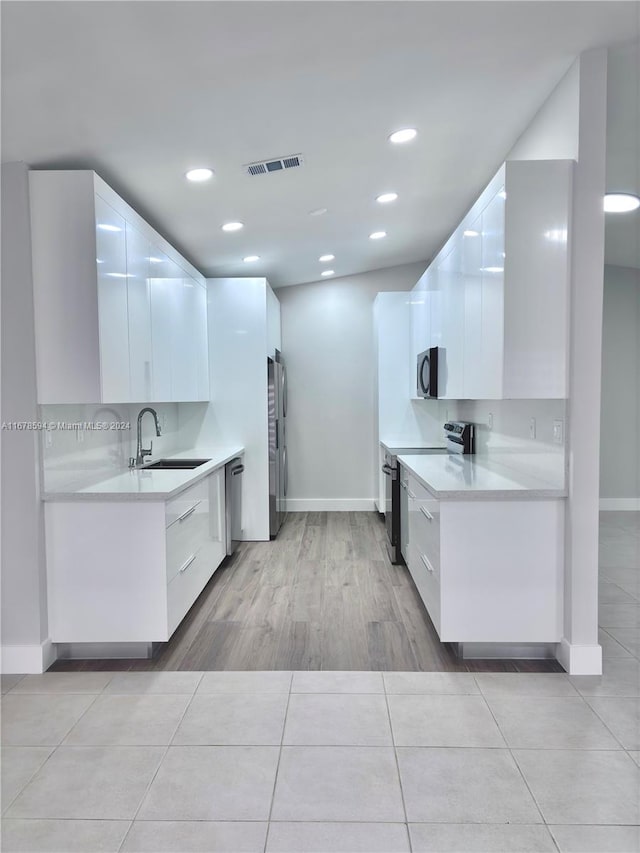 kitchen with appliances with stainless steel finishes, white cabinets, and light hardwood / wood-style flooring