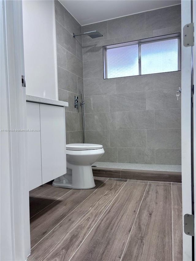 bathroom with a tile shower, toilet, wood-type flooring, and vanity