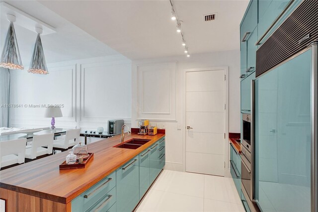 kitchen with rail lighting, light tile patterned floors, butcher block counters, sink, and decorative light fixtures