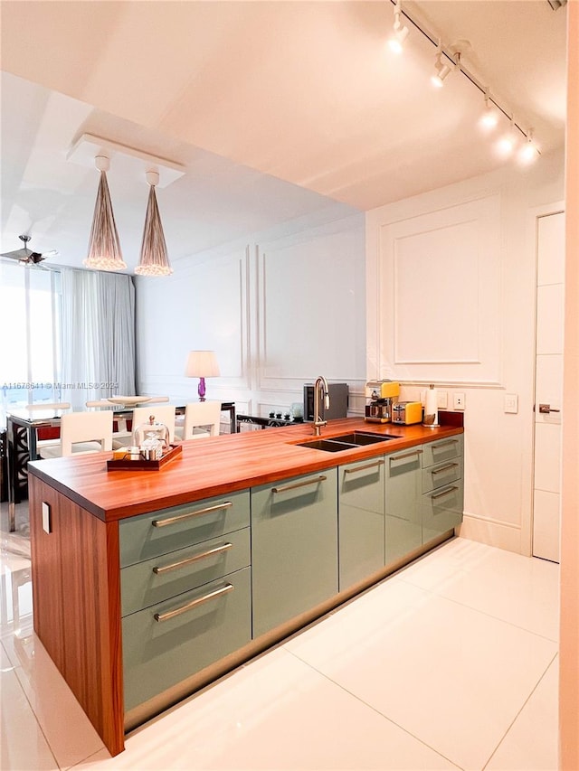 kitchen with ceiling fan, sink, decorative light fixtures, green cabinetry, and butcher block countertops