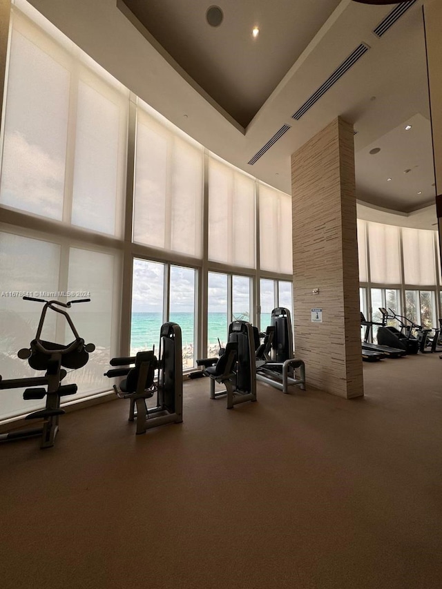 exercise room featuring a water view, a towering ceiling, and floor to ceiling windows