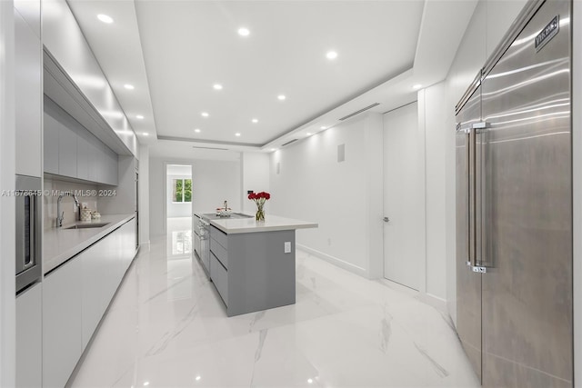 kitchen with stainless steel built in refrigerator, a kitchen island with sink, sink, and gray cabinetry