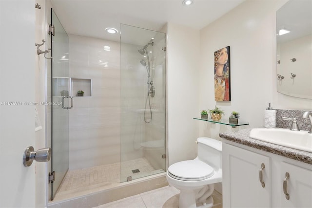 bathroom featuring toilet, vanity, tile patterned floors, and a shower with door