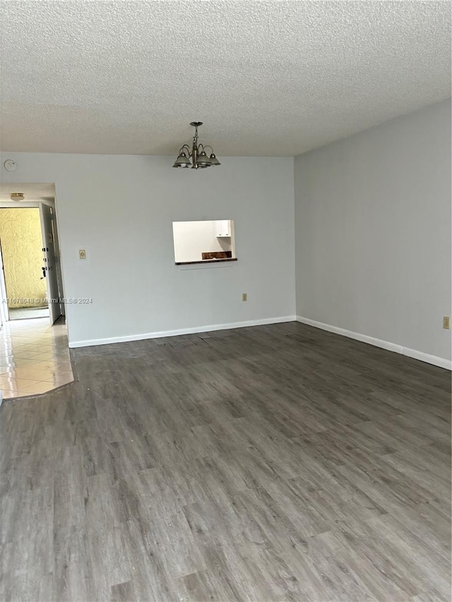 spare room with a textured ceiling, dark hardwood / wood-style flooring, and an inviting chandelier