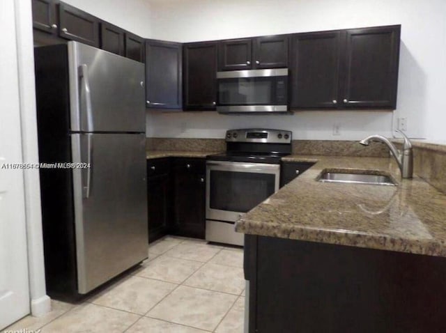 kitchen with stainless steel appliances, dark brown cabinets, sink, light tile patterned flooring, and light stone counters