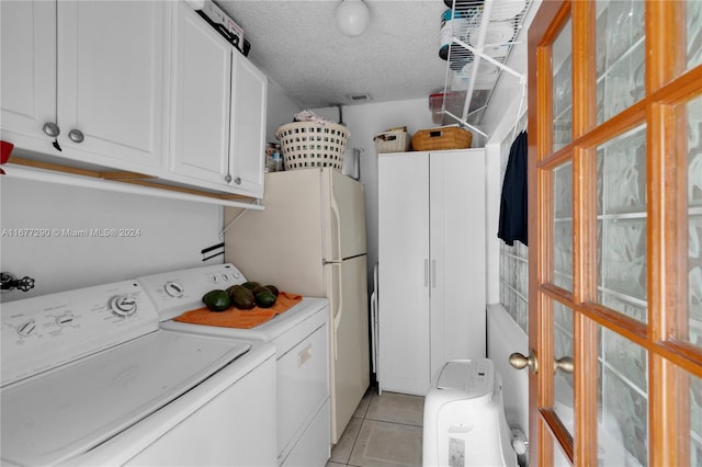 washroom with a textured ceiling, washing machine and dryer, light tile patterned flooring, and cabinets