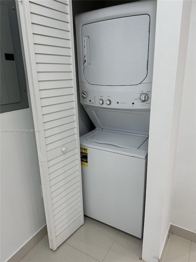 laundry area with stacked washer / drying machine, electric panel, and light tile patterned floors