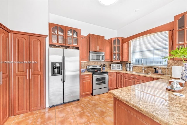 kitchen featuring appliances with stainless steel finishes, sink, light stone counters, decorative backsplash, and light tile patterned floors