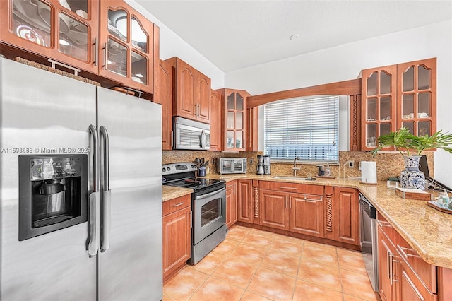 kitchen with tasteful backsplash, light stone countertops, stainless steel appliances, and sink