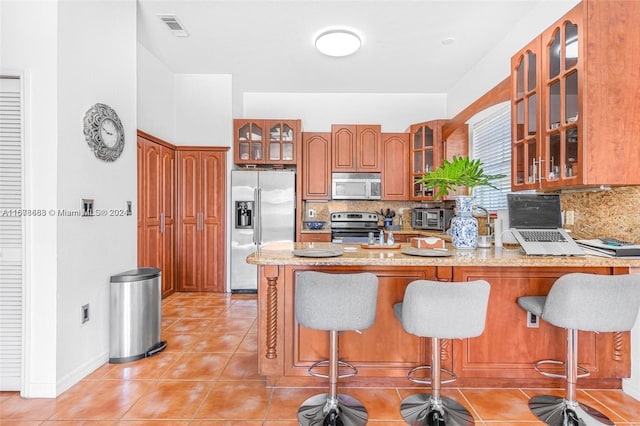 kitchen featuring a breakfast bar, appliances with stainless steel finishes, kitchen peninsula, and tasteful backsplash