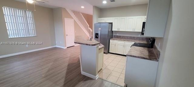 kitchen with black range oven, stainless steel fridge, white cabinets, light hardwood / wood-style floors, and ceiling fan