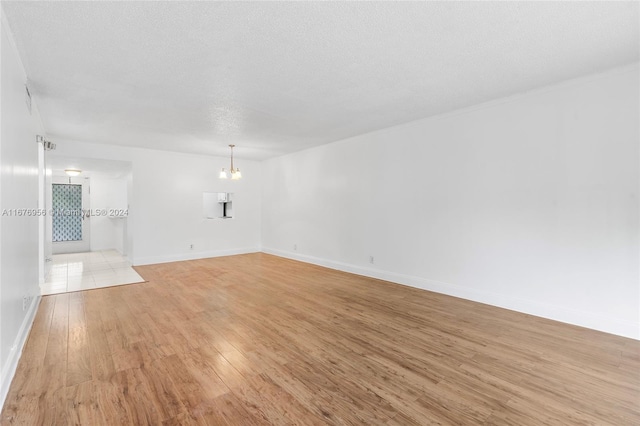 empty room featuring light hardwood / wood-style floors, a notable chandelier, and a textured ceiling