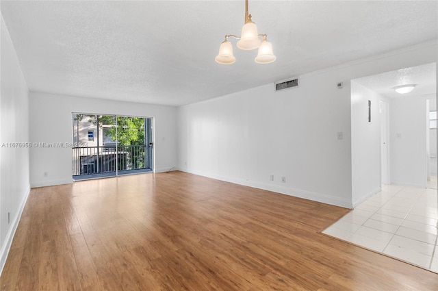 spare room featuring light hardwood / wood-style flooring, a notable chandelier, and a textured ceiling