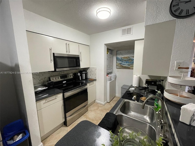 kitchen featuring stacked washer and clothes dryer, sink, light tile patterned floors, appliances with stainless steel finishes, and a textured ceiling