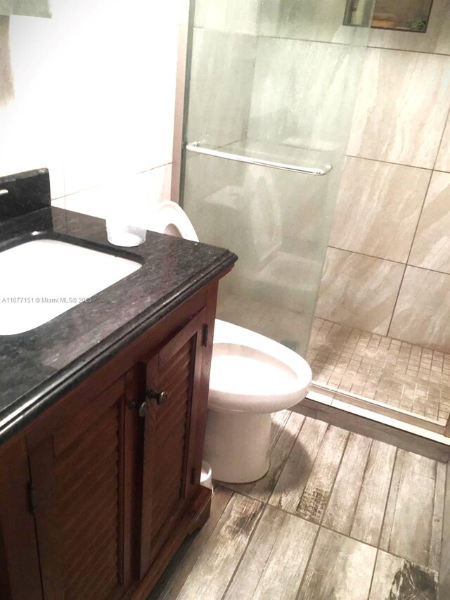 bathroom featuring wood-type flooring, vanity, toilet, and tiled shower