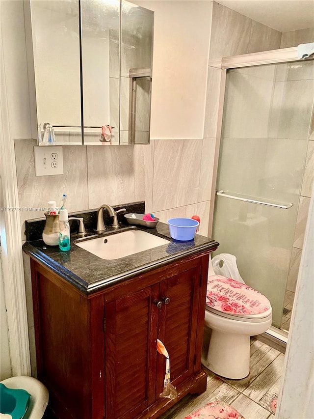 bathroom featuring a shower with shower door, wood-type flooring, tile walls, vanity, and toilet