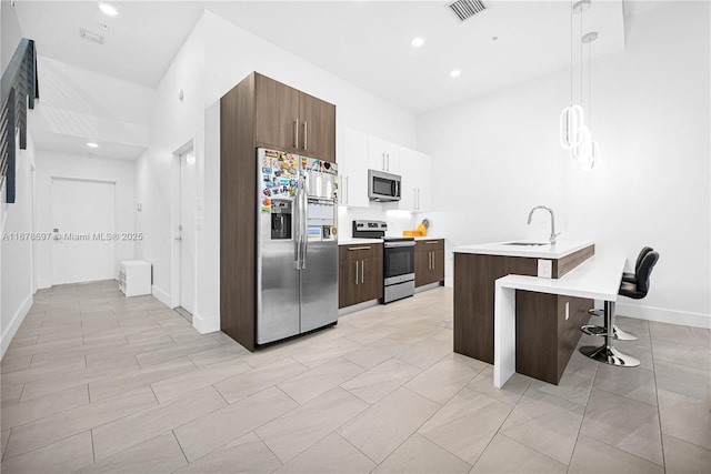 kitchen with sink, pendant lighting, a kitchen bar, a kitchen island with sink, and appliances with stainless steel finishes