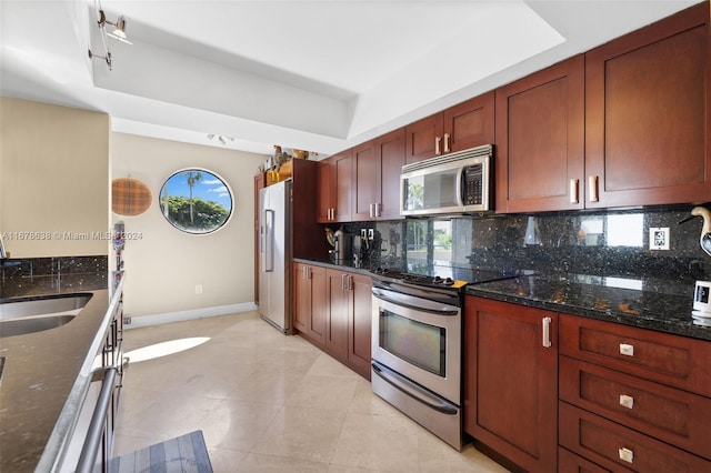 kitchen with backsplash, stainless steel appliances, dark stone counters, and a raised ceiling