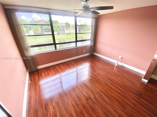 spare room with ceiling fan, a textured ceiling, dark hardwood / wood-style floors, and a water view