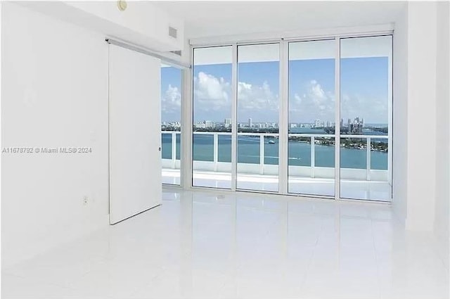 empty room with a wall of windows, tile patterned floors, and a water view