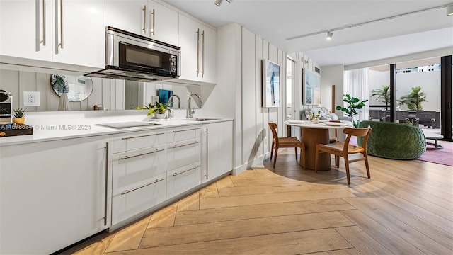 kitchen featuring white cabinets, track lighting, light hardwood / wood-style flooring, black electric stovetop, and sink