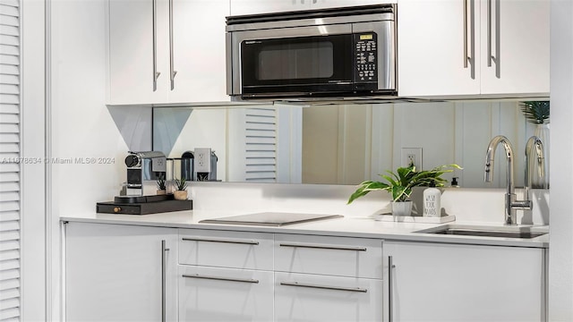 kitchen with black electric stovetop, white cabinetry, and sink