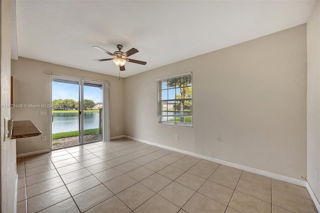 tiled empty room with a healthy amount of sunlight, a water view, and ceiling fan