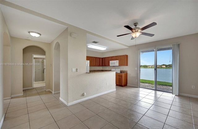 kitchen with light tile patterned flooring, kitchen peninsula, a water view, and white appliances